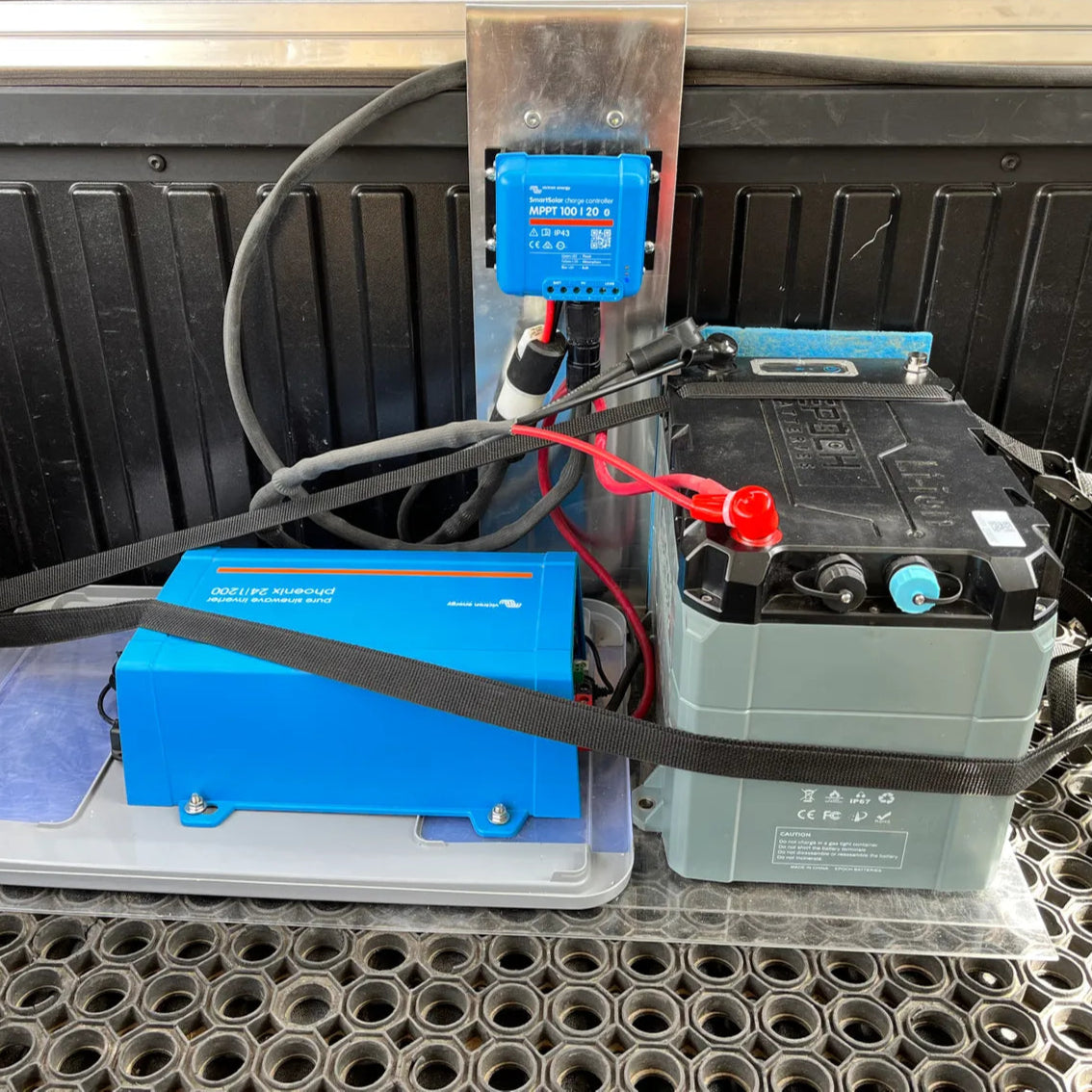 Battery system with blue battery charger and red cables on a vehicle's bed.